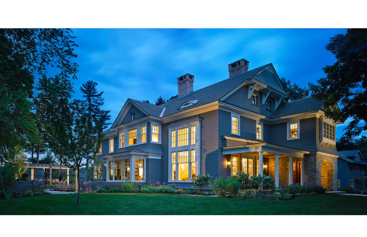 large shingle style home at night with the light on inside